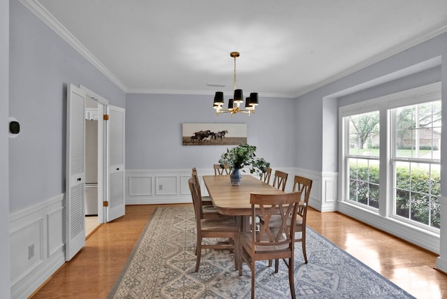 dining area with a chandelier, crown molding, wainscoting, light wood-style floors, and a decorative wall