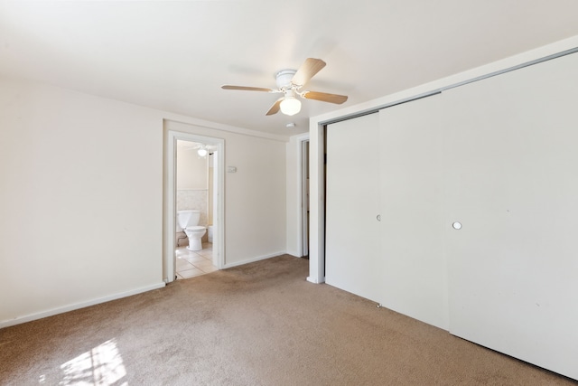 unfurnished bedroom featuring light colored carpet, ceiling fan, baseboards, a closet, and ensuite bath