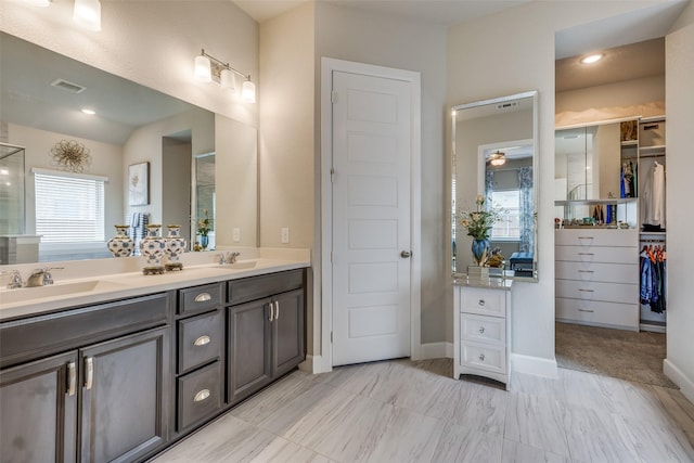 full bathroom with double vanity, a walk in closet, a ceiling fan, and a sink