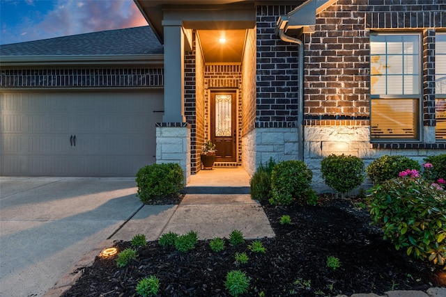 property entrance with brick siding, a shingled roof, driveway, and an attached garage