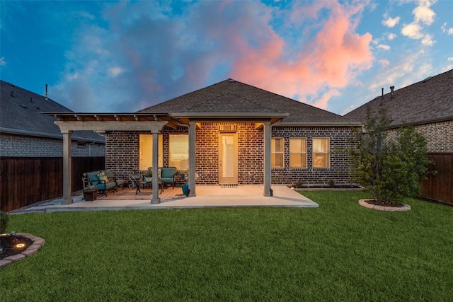 back of house at dusk with a patio area, a shingled roof, a lawn, brick siding, and a fenced backyard