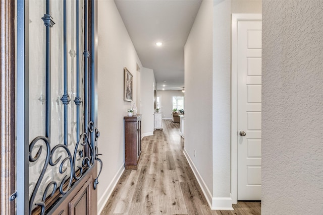 corridor with a textured wall, light wood-type flooring, recessed lighting, and baseboards