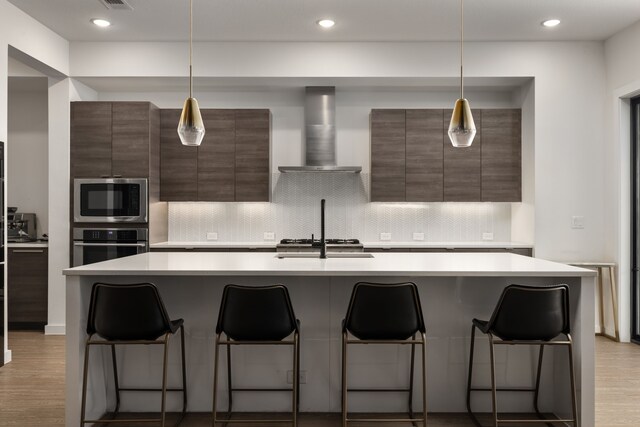 kitchen featuring wall chimney range hood, stainless steel appliances, light countertops, and modern cabinets