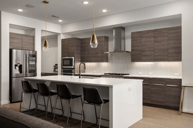 kitchen featuring a sink, a breakfast bar, stainless steel appliances, wall chimney exhaust hood, and modern cabinets