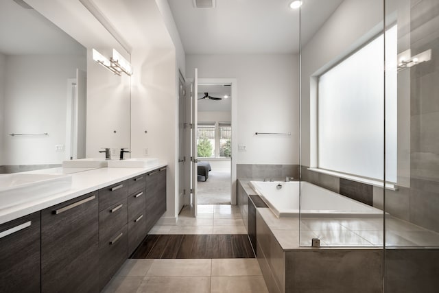 ensuite bathroom featuring a sink, double vanity, a bath, tile patterned floors, and a ceiling fan
