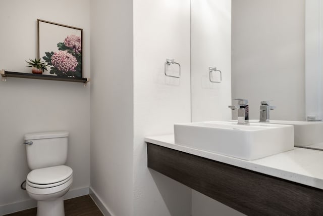 bathroom with baseboards, wood finished floors, toilet, and vanity