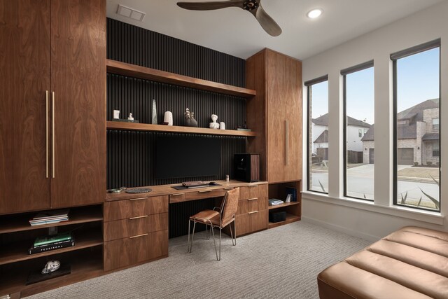 home office with light colored carpet, built in desk, ceiling fan, baseboards, and visible vents