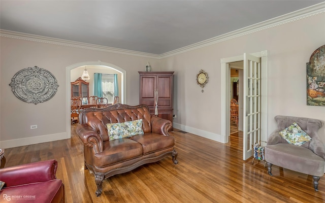 living room featuring baseboards, arched walkways, crown molding, and wood finished floors