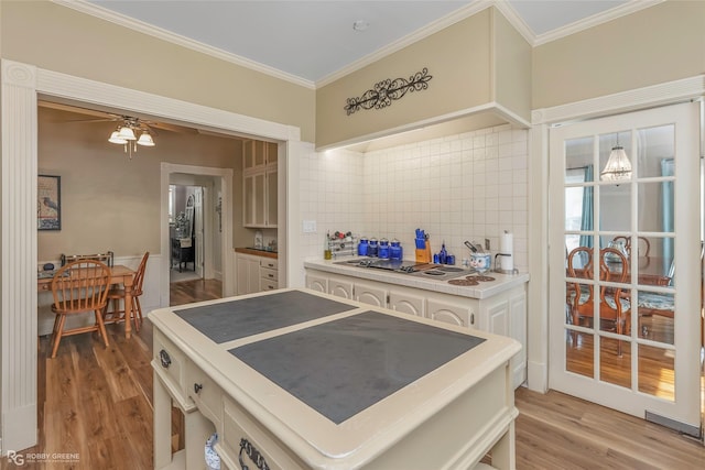 kitchen featuring crown molding, light wood-style floors, light countertops, cooktop, and backsplash