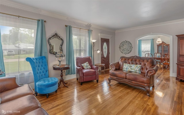 living area featuring light wood-style floors, ornamental molding, and arched walkways