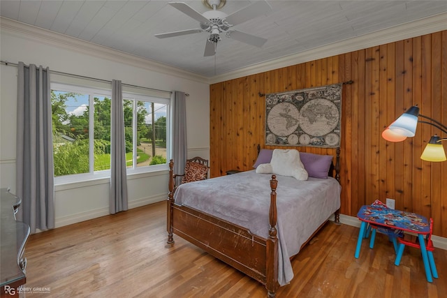 bedroom with ceiling fan, crown molding, wood walls, wood finished floors, and baseboards