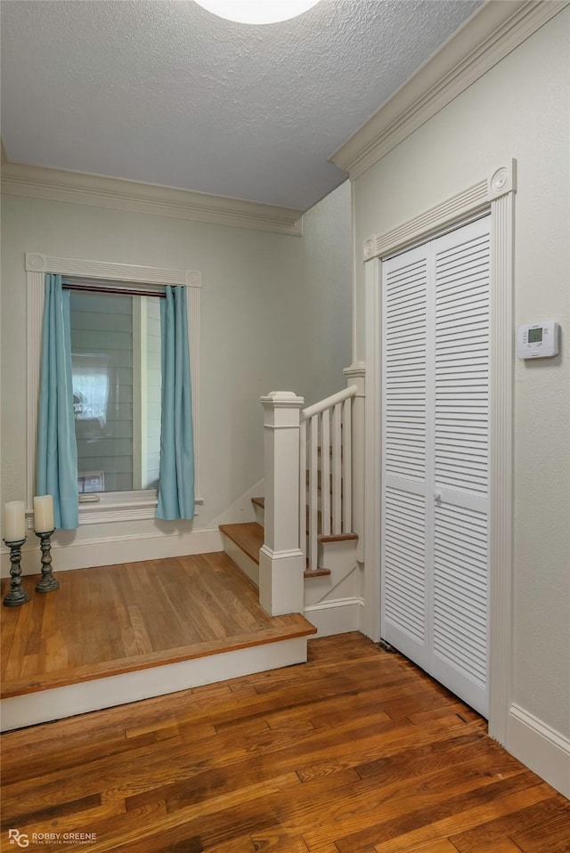 stairs with ornamental molding, a textured ceiling, and wood finished floors