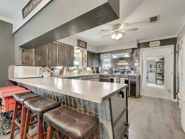 kitchen with crown molding, visible vents, a peninsula, white microwave, and a ceiling fan