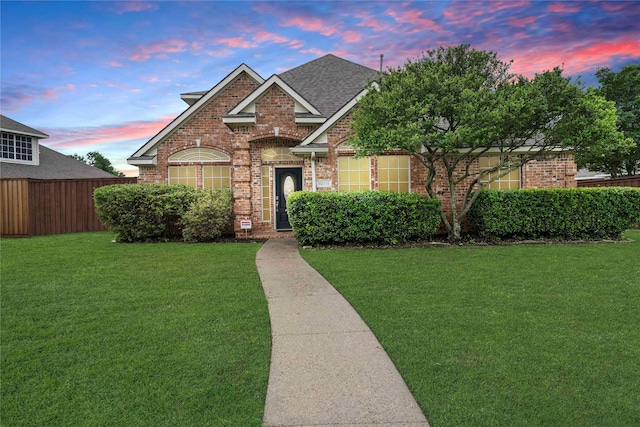 traditional-style home with brick siding, roof with shingles, fence, and a front yard