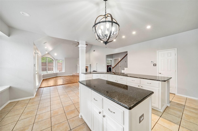 kitchen featuring decorative columns, a center island, light tile patterned floors, baseboards, and a notable chandelier