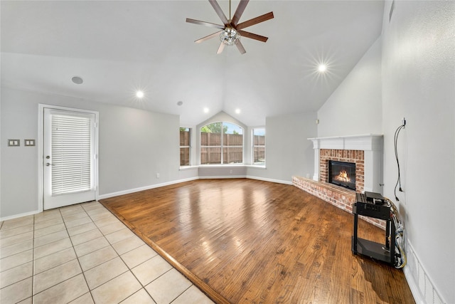 unfurnished living room featuring ceiling fan, tile patterned flooring, a brick fireplace, baseboards, and lofted ceiling