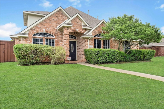 view of front facade featuring brick siding, fence, roof with shingles, and a front lawn