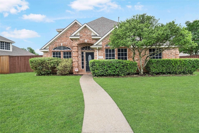 view of front of home with fence, roof with shingles, a front lawn, and brick siding