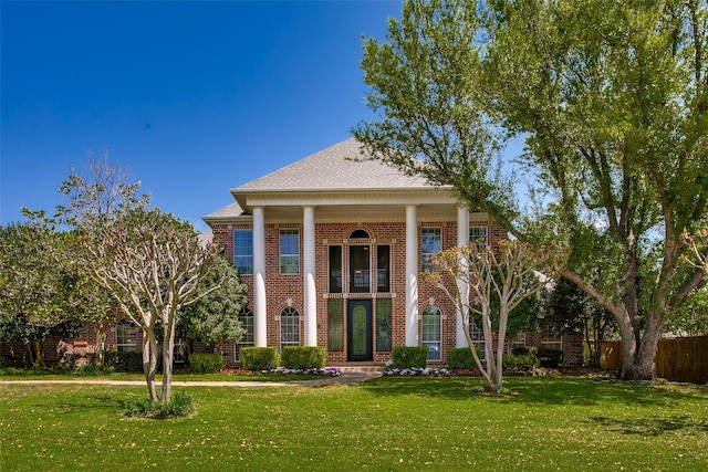 greek revival house featuring brick siding, fence, and a front yard