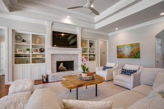 living room with a tray ceiling, ornamental molding, a fireplace, and a ceiling fan