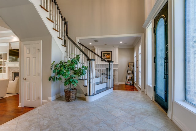entrance foyer with stairway, baseboards, ornamental molding, and a fireplace