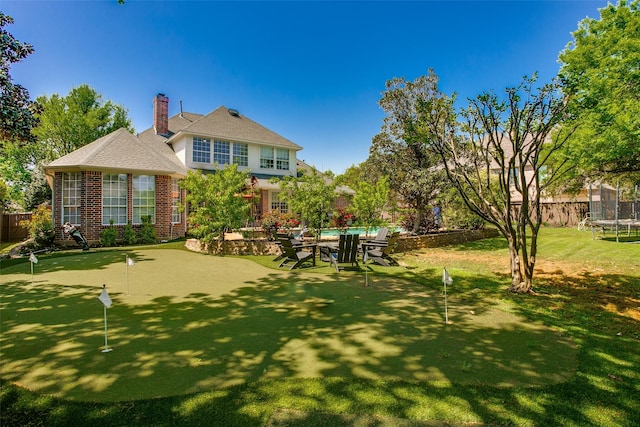 back of house with fence, a trampoline, brick siding, a fenced in pool, and a chimney