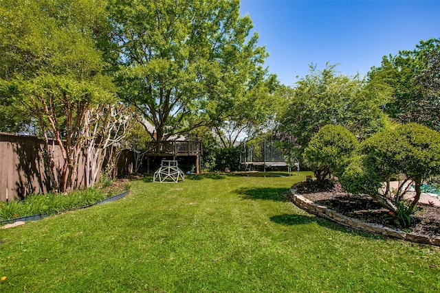 view of yard featuring fence, a wooden deck, and a trampoline