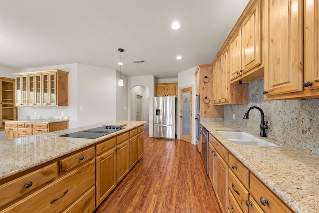 kitchen featuring light stone countertops, a sink, arched walkways, appliances with stainless steel finishes, and wood finished floors