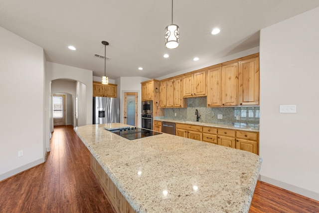 kitchen featuring dark wood finished floors, arched walkways, a spacious island, stainless steel appliances, and a sink