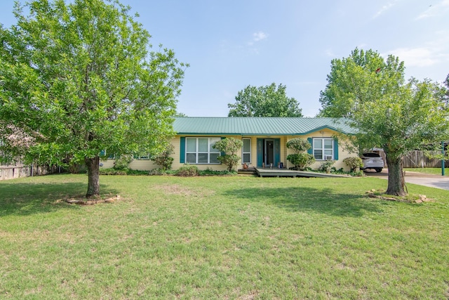 ranch-style home featuring fence, a carport, metal roof, and a front lawn