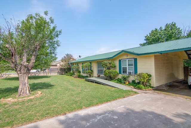 view of front of home with a front yard, an attached carport, metal roof, aphalt driveway, and fence