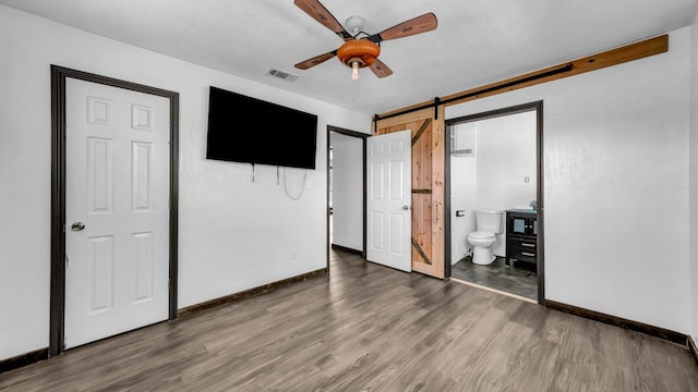 760 College Farm, Stephenville, TX 76401 - unfurnished bedroom featuring connected bathroom, visible vents, a barn door, baseboards, and wood finished floors
