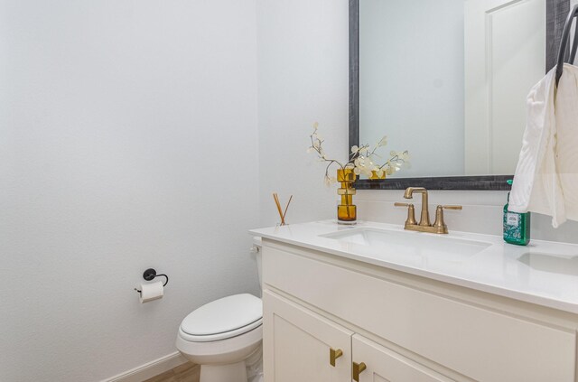 half bathroom featuring vanity, baseboards, toilet, and wood finished floors