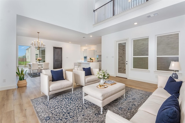living area with light wood-style floors, a towering ceiling, visible vents, and a chandelier