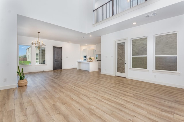 unfurnished living room featuring light wood finished floors, a chandelier, baseboards, a towering ceiling, and visible vents