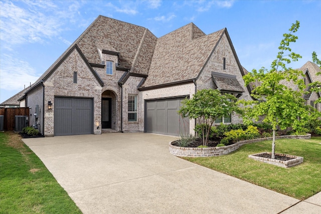 french country inspired facade with central AC, brick siding, a garage, and concrete driveway
