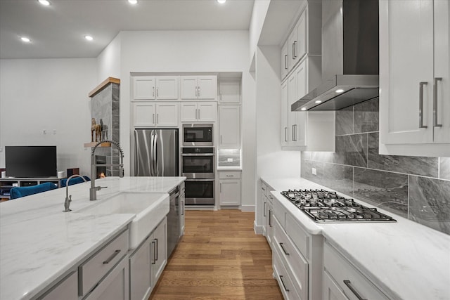 kitchen featuring wall chimney range hood, a sink, light stone countertops, and appliances with stainless steel finishes