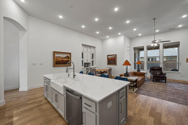 kitchen with a sink, dishwasher, light wood finished floors, a center island with sink, and gray cabinets