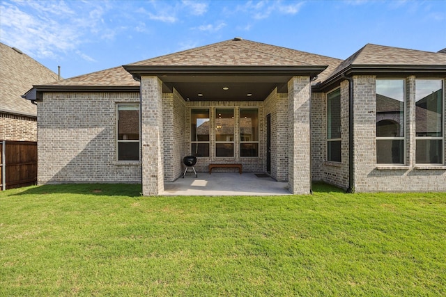 back of house featuring brick siding, fence, roof with shingles, a patio area, and a lawn