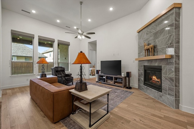 living area featuring a tiled fireplace, a ceiling fan, visible vents, baseboards, and wood finished floors