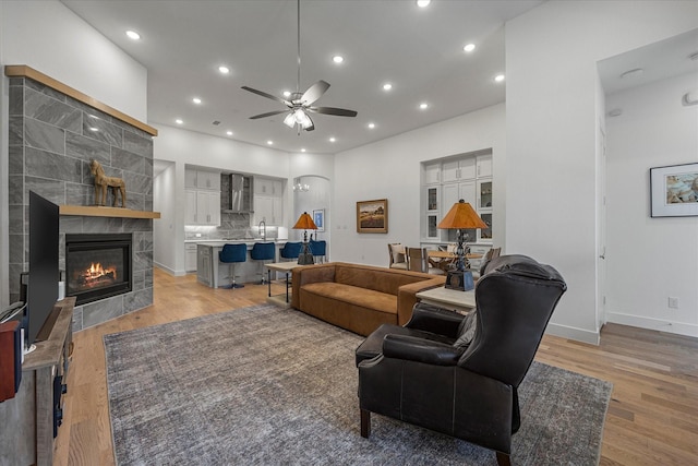 living room with a ceiling fan, a tile fireplace, light wood-style flooring, and recessed lighting