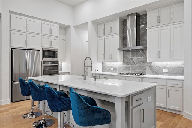 kitchen featuring tasteful backsplash, light stone countertops, light wood-style floors, appliances with stainless steel finishes, and wall chimney exhaust hood