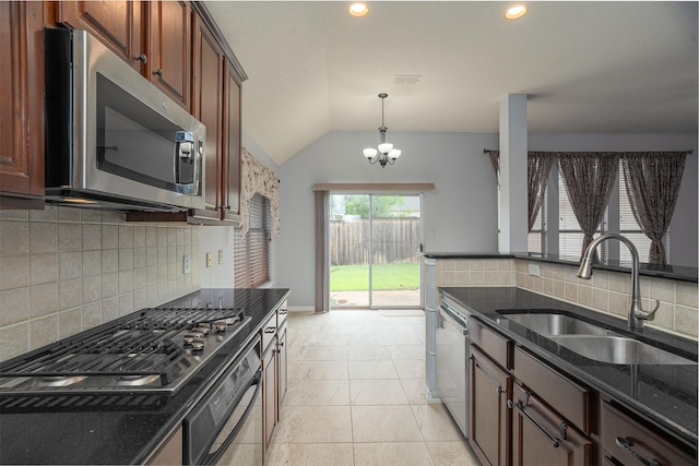 kitchen featuring lofted ceiling, dark stone counters, decorative backsplash, a sink, and appliances with stainless steel finishes