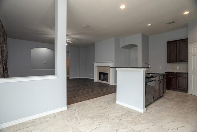 kitchen featuring a tiled fireplace, arched walkways, a sink, a ceiling fan, and dishwashing machine
