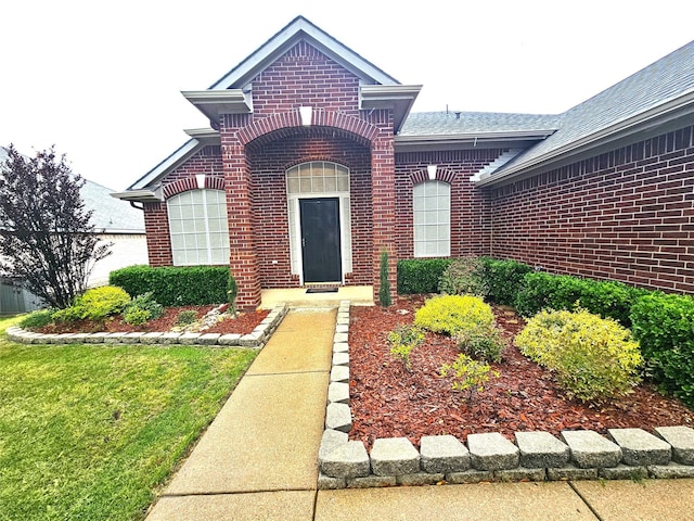doorway to property with brick siding and a shingled roof