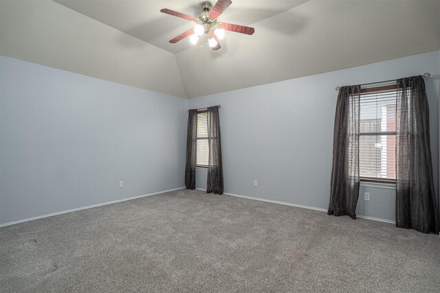 empty room with a healthy amount of sunlight, a ceiling fan, carpet flooring, and vaulted ceiling