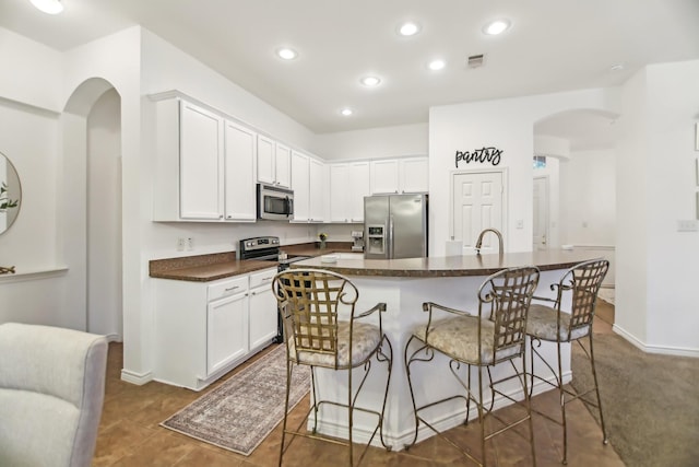 kitchen featuring dark countertops, a breakfast bar area, white cabinetry, arched walkways, and stainless steel appliances