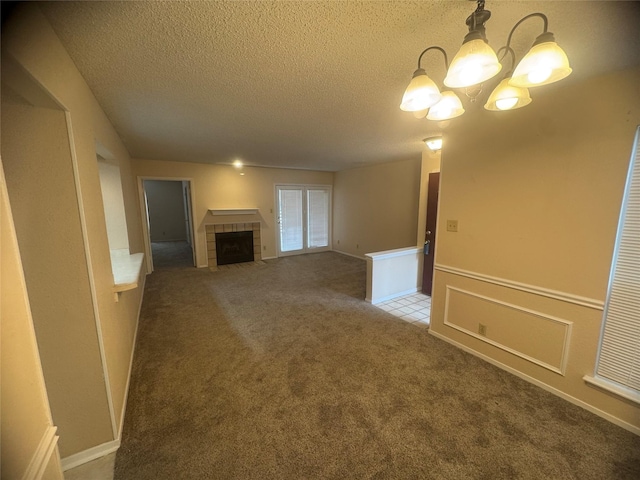 unfurnished living room with a textured ceiling, a chandelier, a tiled fireplace, and carpet flooring