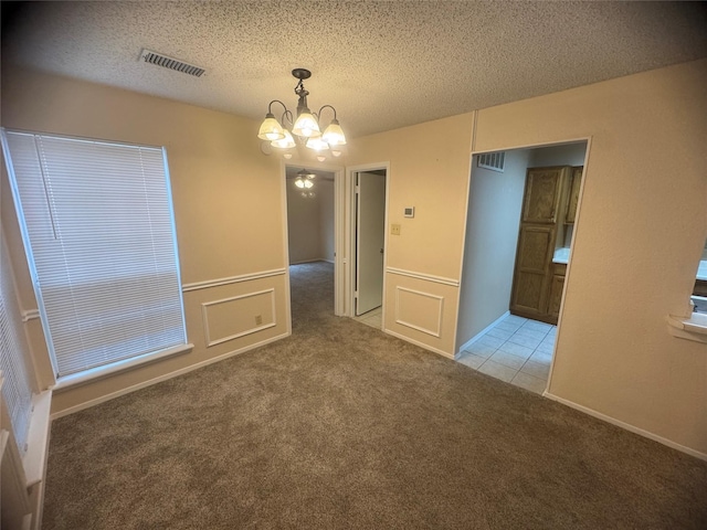 unfurnished room with carpet flooring, an inviting chandelier, visible vents, and a textured ceiling