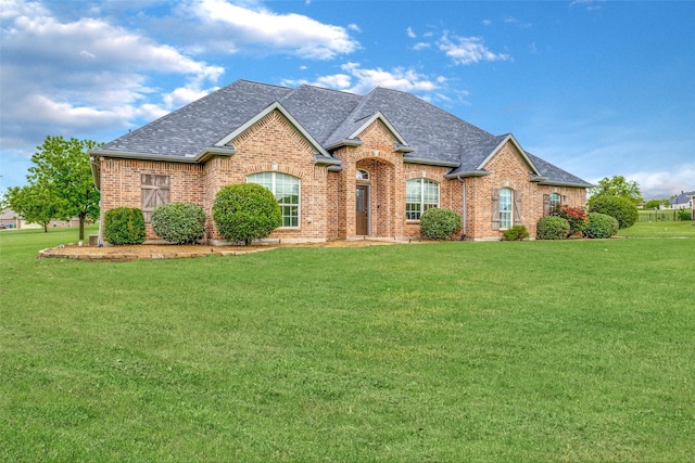 view of front facade featuring a front yard, roof with shingles, and brick siding